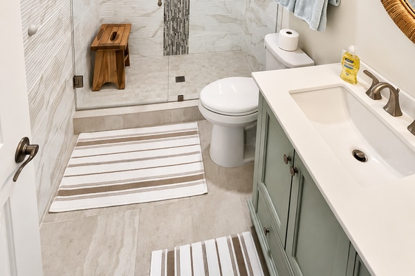 Modern bathroom with shower, vanity, toilet, and striped rugs