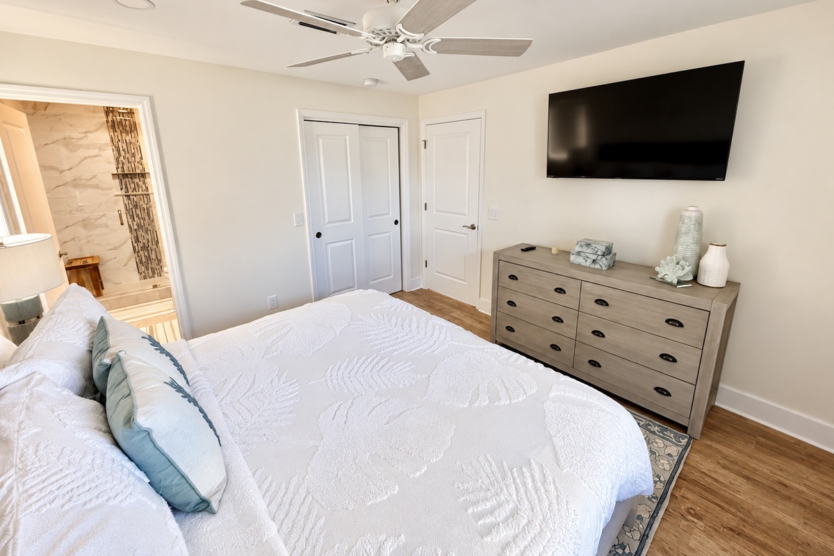 Bright bedroom with bed, dresser, TV, and ensuite bathroom